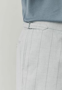 Hellgraue, taillierte Hose mit vertikalen Nadelstreifen, die eine glatte Textur aufweist, seitliche Taschen hat und einen eleganten, verstellbaren Gürtel in der Taille bietet.