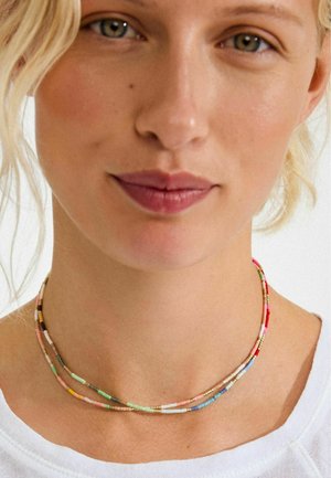 Kralenketting met meerdere strengen in pasteltinten, voorzien van kleine gouden accenten, gedragen rond de hals over een lichtgekleurde blouse.