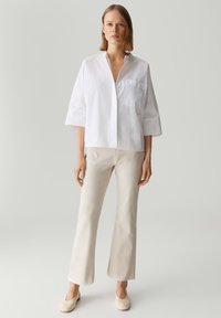 Witte, gestructureerde katoenenshirt met een kraag, halve mouwen en een borstzak, gecombineerd met beige, flared broeken en lichte schoenen.