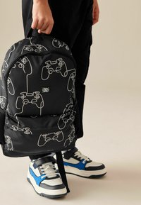Schwarzer Rucksack mit einem Muster aus weißen Gaming-Controllern, aus strapazierfähigem Stoff gefertigt. Mit einem Griff und verstellbaren, gepolsterten Schultergurten.