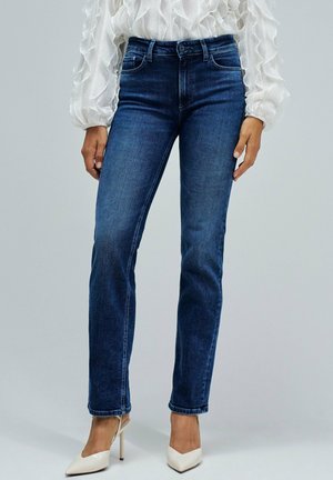 Vaqueros de mezclilla azul oscuro con un corte recto, diseño de cinco bolsillos y costuras visibles. Combinados con zapatos de tacón beige.