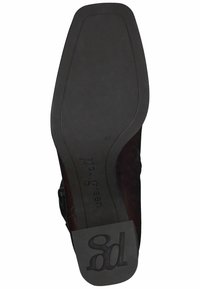 Suela de zapato de ante marrón con goma negra texturizada. Presenta una marca en relieve y una forma distintiva, con un borde liso y un ligero tacón.