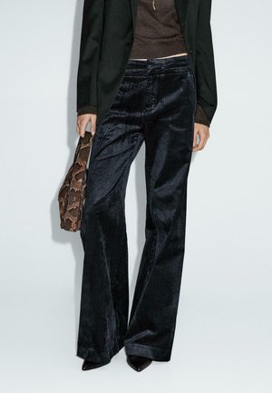 Person wearing black corduroy wide-leg pants, black blazer, brown top, black pointed shoes, holding a brown snakeskin-patterned bag.