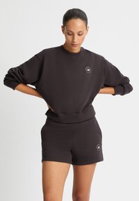 Felpa nera in cotone con spalle scese, polsini a costine e un piccolo logo. Abbinata a pantaloni corti neri coordinati, anch'essi in cotone.