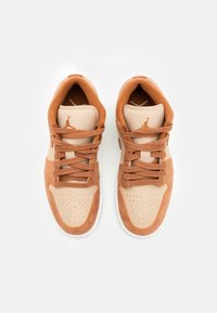 Une paire de baskets beiges et brunes à lacets avec des embouts perforés et un logo sur les languettes rembourrées, vue d'en haut sur un fond blanc.