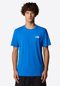 Blå t-shirt med rund hals gjord av bomull, med korta ärmar och en liten vit logotyp på vänstra bröstet. Slät textur, avslappnad passform.