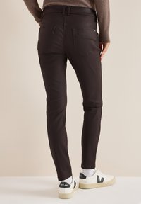 Černé slim-fit kalhoty s středním pasem, dvěma zadními kapsami a hladkým povrchem. V kombinaci s bílými teniskami.