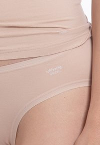 Lättviktig sömlös underkläder i beige med mjukt tyg, elastiskt midjeband och tryckt logotyp på midjebandet. Slät textur, minimal design.