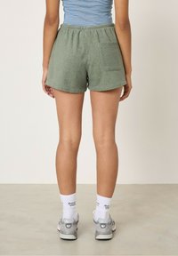 Pantaloni corti in spugna verde con cintura elastica, dotati di una tasca posteriore. Indossati con calzini bianchi e scarpe sportive grigie.