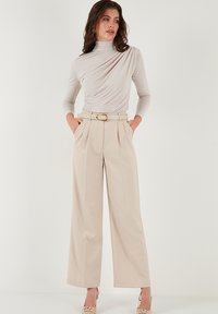 Lichtbeige coltrui met gedrapeerd ontwerp, gecombineerd met high-waisted wijde broek en een bijpassende riem met een gouden gesp.