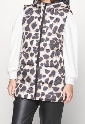 Kamizelka puchowa bez rękawów z czarno-beżowym nadrukiem w panterkę, noszona na białej bluzce z długim rękawem i czarnych skórzanych spodniach.