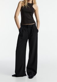 Black wide-leg trousers with pleats and a belted waist paired with a fitted dark tank top. The fabric appears smooth with a structured design.