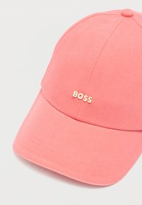 Różowa czapka bejsbolowa z bawełny, z zakrzywionym daszkiem i wypukłym złotym logo "BOSS" z przodu. Gładka faktura i wyraźnie ukształtowany kształt.