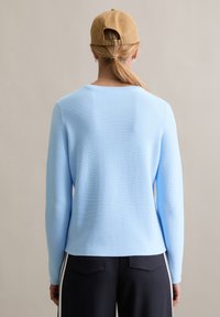 Lichtblauwe geribbelde trui met lange mouwen, ronde hals en een losse pasvorm, gecombineerd met zwarte broek met witte zijstrepen.