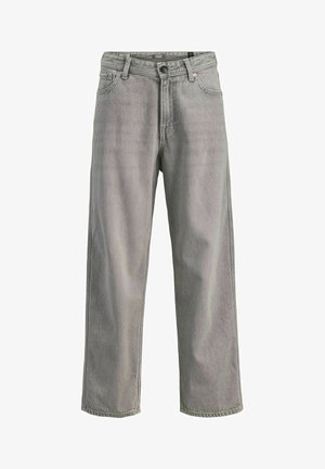 Poiss seisab, vaadates paremale, seljas helesinine trükitud T-särk, laiad hallid püksid ja valged tossud lihtsal heledal taustal.