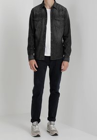 Mörk denimskjorta med två bröstfickor, kombinerad med en vit T-shirt, marinblå byxor och ljusgrå sneakers. Enkel, skräddarsydd passform.