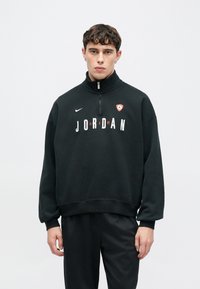 Μαύρο φλις φούτερ με φερμουάρ στο ένα τέταρτο, με λευκή και κόκκινη εκτύπωση "JORDAN" και λογότυπο Nike. Διαθέτει άνετη εφαρμογή και ριμπ μανσέτες.
