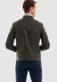Mörk läderjacka med texturerade paneler, en ljusgrå krage och en figurnära design. Har en ren sömsstruktur och minimal hårdvara.