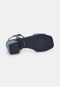 Mustad musta kontsaga sandaal, millel on paks plokknina ja reguleeritav pahkluu rihm. Omab tekstuuriga talla ja sileda ülemise materjali mugavuse jaoks.