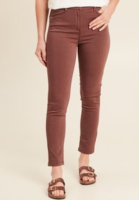 Bruine slim-fit jeans met een gladde textuur en een gemiddelde taille. Voorzien van ritszakken en een opgerolde zoom. In combinatie met bruine sandalen.