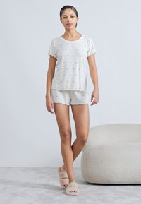 Σετ πιτζάμας σε ανοιχτό γκρι χρώμα που περιλαμβάνει μπλούζα με κοντά μανίκια, διακοσμημένη με κόκκινα σχέδια καρδιάς και άκρες με κυματιστό μοτίβο, συνοδευόμενη από σορτς στο ίδιο σχέδιο. Απαλή υφή.