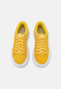 Gula mockasinsneakers med vita gummisålar, försedda med matchande gula snörningar och en texturerad innersula med ett geometriskt mönster.