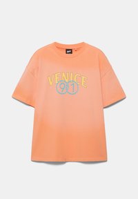 T-shirt à manches courtes couleur pêche avec le texte jaune "VENICE" et des cercles bleus en pointillés autour de "901" à l'avant, présenté sur fond blanc.