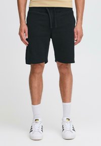 Pantalones cortos de algodón negros con cintura elástica y cordón, con bolsillos laterales, que terminan justo por encima de la rodilla. Se llevan con calcetines blancos y zapatillas.