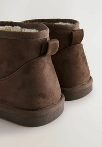 Pruun sametist pahkluu saapad on pehme vooder, ümar kuju ja väike konts; sisaldavad tekstuurilisi detaile ja tikitud tallat.