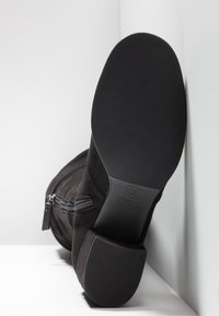 Bottine en daim noir avec bout arrondi, fermeture éclair latérale et semelle en caoutchouc texturée. Le talon est bas et épais pour plus de stabilité.