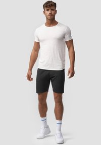 Hvid T-shirt med korte ærmer kombineret med mørkegrå shorts. Modellen har hvide sneakers med blå accenter og hvide sokker på. Simpelt, afslappet design.