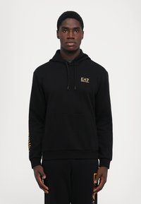 Zwarte hoodie met een kangoeroezak, opgestikte mouwen en een gouden EA7-logo op de borst. Soepele textuur met een ontspannen pasvorm.