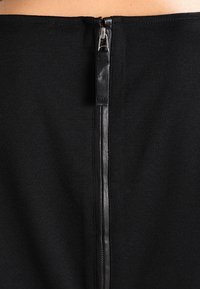 Robe en tricot noir avec une fermeture éclair au dos, équipée d'un tirette noir mat, intégrée harmonieusement dans le design du vêtement.