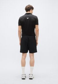 Juoda polo marškinėliai ir juodos kelnės, abu pagaminti iš minkštos medžiagos. Marškinėliuose gale yra subtilus logotipas, ribotais apykaklės kraštais ir rankovėmis.