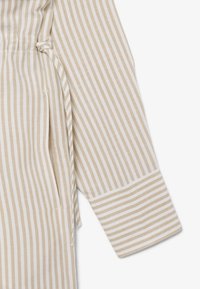 Beiges und weißes, vertikal gestreiftes Langarmoberteil mit Manschetten und einem gebundenen Stoffgürtel in Taillennähe.