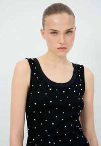 Svart linne med rundad halsringning och spridda silverdetaljer. Tyget har en slät textur och ger en figursydd silhuett.
