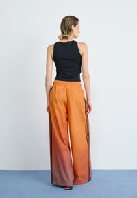 Melnā bez piedurknēm topa kombinācija ar oranžām ombre brīva piegriezuma biksēm, kas apakšpusē ir melnas sānu svītras. Gluda auduma konstrukcija ar elastīgu jostas detaļu.