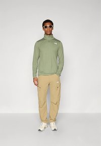 Lichtgroen shirt met lange mouwen en rits, met kraag, gecombineerd met beige cargobroek met zijzakken, en witte sneakers.