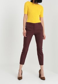 Yellow ribbed short-sleeve top paired with burgundy tailored trousers and brown leopard-print high heels, showcasing a fitted silhouette.