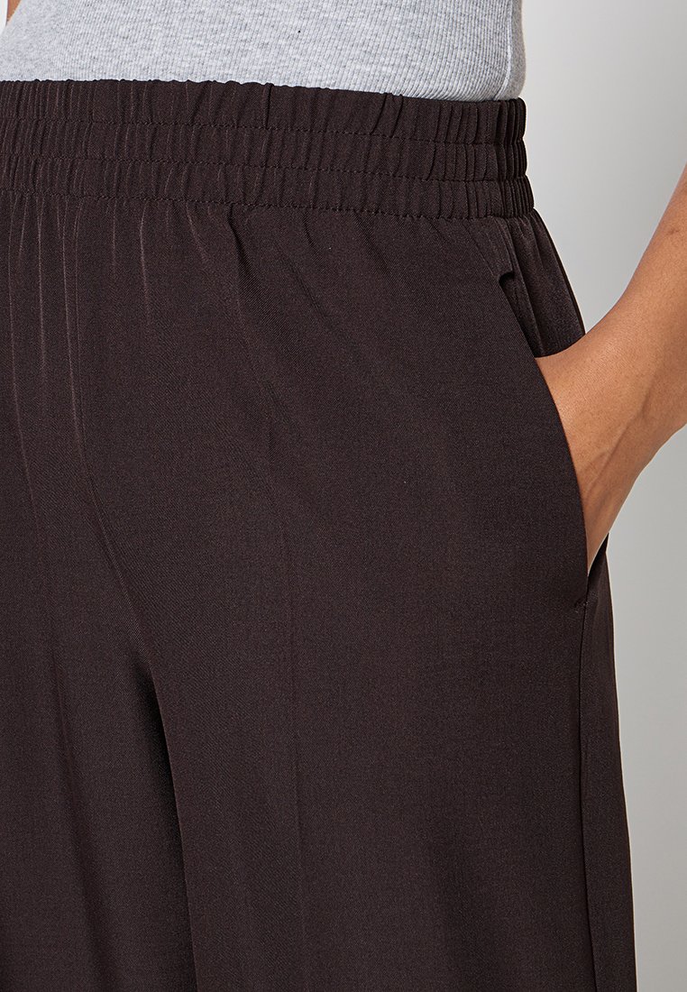 Zwarte, wijde broek van zachte stof met een elastische tailleband en zijzakken. Soepele textuur, getailleerde pasvorm en subtiele plooien.