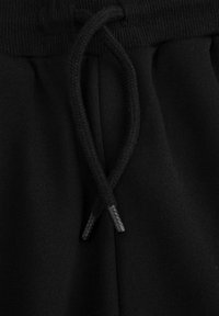 Czarne dresy z elastycznym sznurkiem w pasie. Miękka tekstura z elastycznymi ściągaczami na mankietach. Prosty i minimalistyczny design.