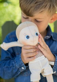 Zachte stoffen pop met een beige hoofd, gestreept shirt en witte shorts. Voorzien van grote blauwe ogen en geborduurde gelaatskenmerken. Kinderhanden houden de pop vast.
