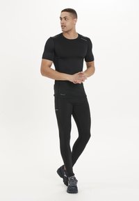 Schwarzes, figurbetontes Sportshirt mit kurzen Ärmeln, kombiniert mit schwarzen Kompressionsleggings mit seitlichem Akzent und schwarzen Sportschuhen.
