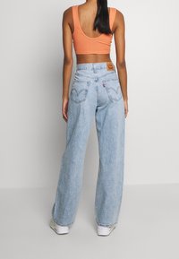 Jeans in denim azzurro chiaro a gamba larga con tasche posteriori prominenti e un'etichetta in pelle sulla vita. Abbinati a un crop top arancione.