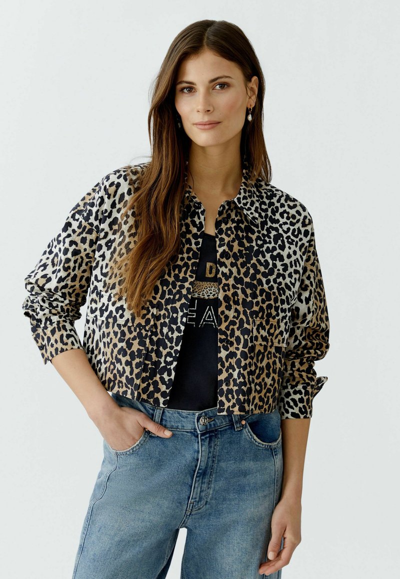 Leopardenmuster cropped Jacke mit Kragen, langen Ärmeln und Knopfverschluss in Beigetönen und Schwarz, kombiniert mit Jeans aus Denim.