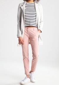 Pantaloni su misura rosa chiaro, cappotto lungo grigio e top corto a righe blu navy con scollatura rotonda, completati da sneakers bianche.