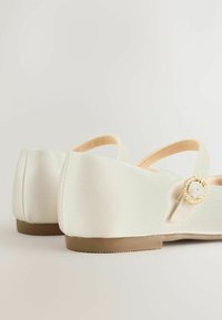 Pantofi din satin culoarea fildeș deschis, cu toc mic, vârf rotund și detaliu decorativ cu cataramă pe curea. Textură netedă și design simplu.