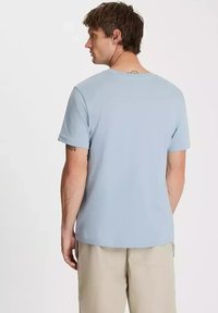 Jasnoniebieska koszulka z krótkim rękawem, okrągłym dekoltem, gładką fakturą i prostym wzorem, noszona z beżowymi szortami. Minimalne detale z tyłu widoczne.