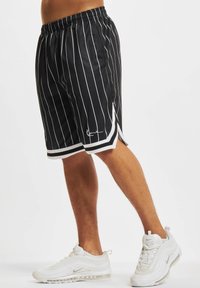 Černé sportovní šortky s bílými svislými pruhy, elastickým pasem a bočními rozparky. Ozdobené bílým lemem a detailním logem.