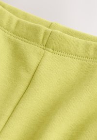 Limettengrüner Baumwollstoff mit weicher Textur, der die obere Naht und die Nähte eines Kleidungsstücks zeigt.